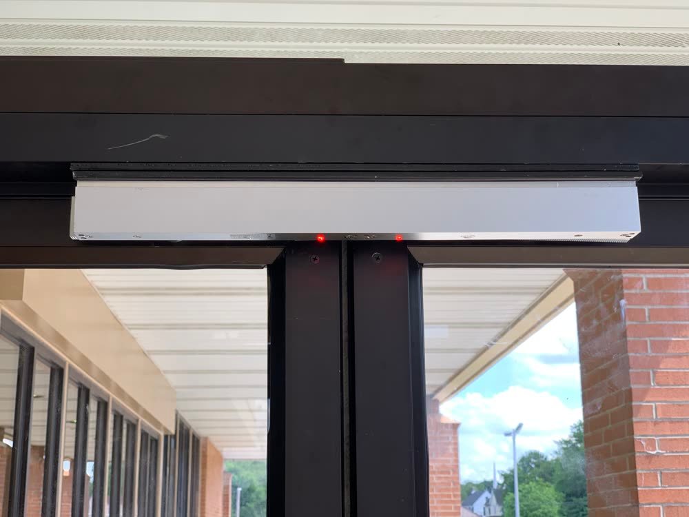 Magnetic lock mounted on the header of a glass entry door, status LEDs lit